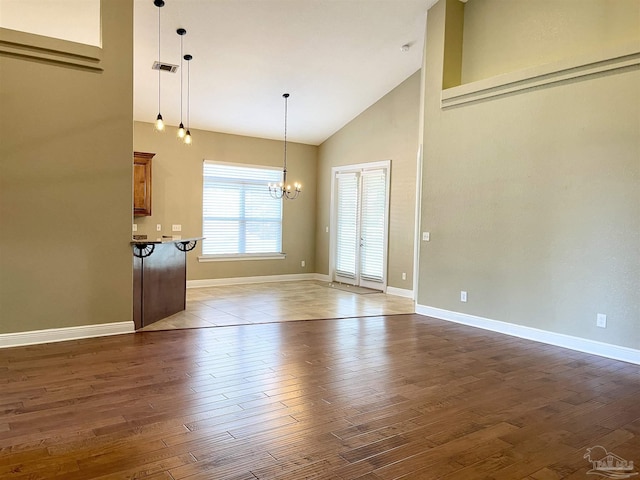 unfurnished living room featuring a chandelier, high vaulted ceiling, visible vents, baseboards, and hardwood / wood-style floors