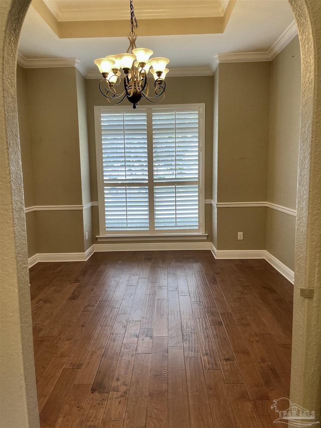 spare room featuring a chandelier, dark wood-type flooring, crown molding, baseboards, and arched walkways