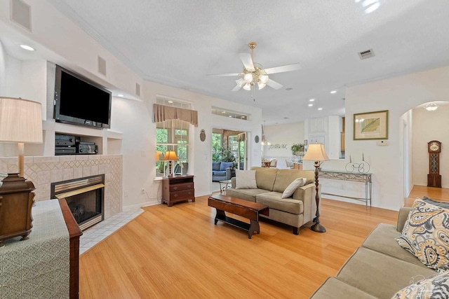 living room with ceiling fan, light hardwood / wood-style floors, a textured ceiling, and a tiled fireplace