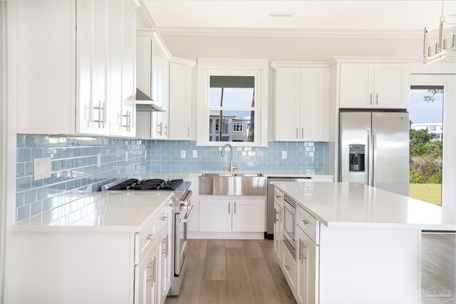 kitchen with stainless steel appliances, white cabinets, sink, light hardwood / wood-style flooring, and decorative light fixtures