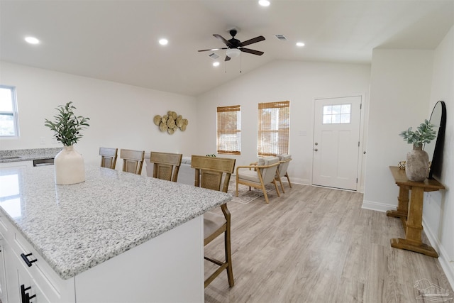 kitchen featuring lofted ceiling, a breakfast bar area, white cabinetry, light hardwood / wood-style flooring, and light stone countertops