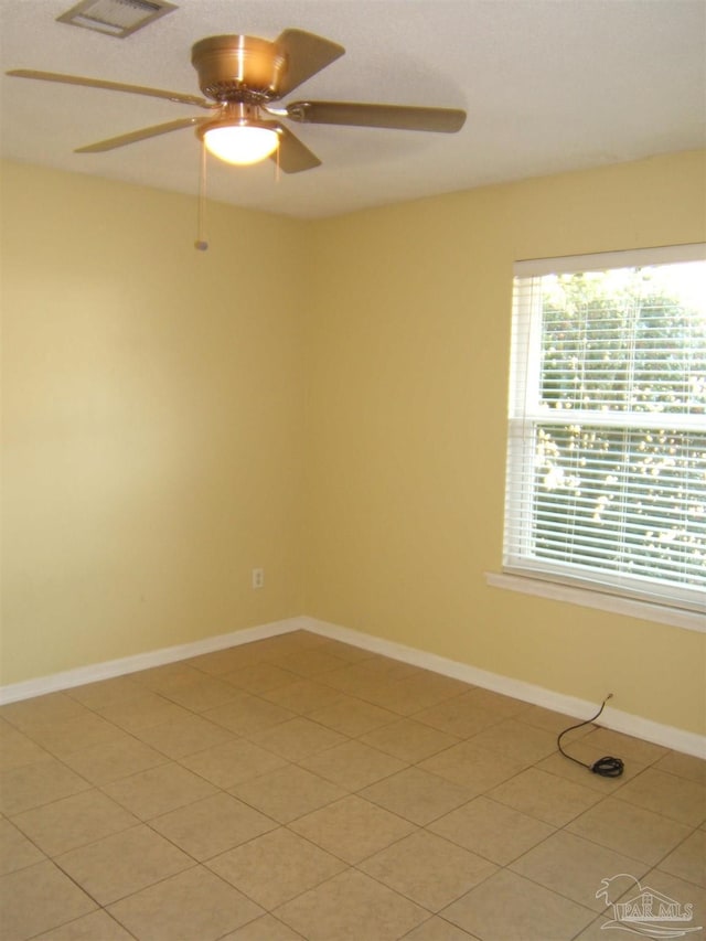 empty room featuring a wealth of natural light, ceiling fan, and light tile patterned floors