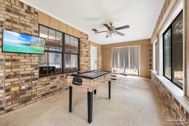 game room with ceiling fan and brick wall