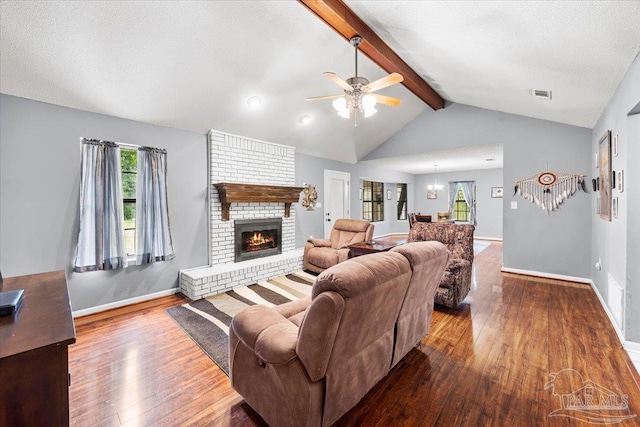 living room with ceiling fan with notable chandelier, a fireplace, a textured ceiling, wood-type flooring, and vaulted ceiling with beams