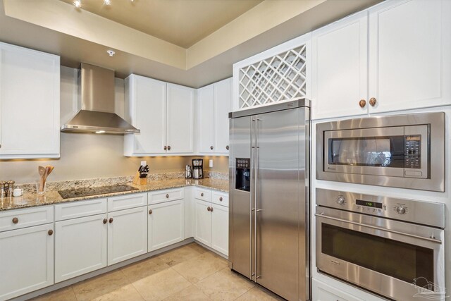 kitchen with white cabinetry, wall chimney range hood, light stone counters, and built in appliances