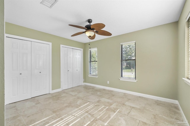 unfurnished bedroom with ceiling fan and multiple closets