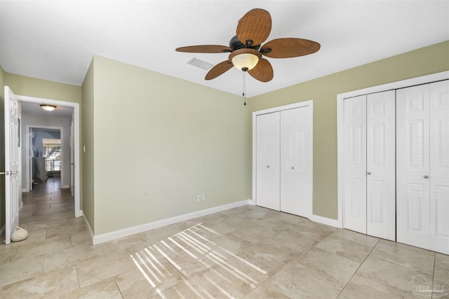 unfurnished bedroom featuring ceiling fan and two closets