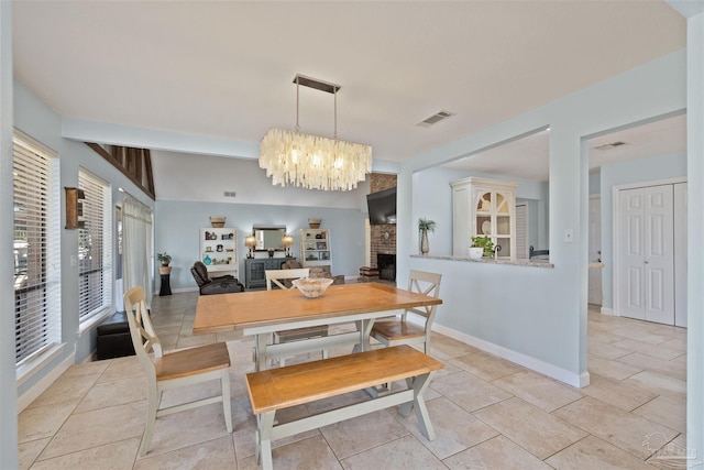 dining area with a notable chandelier, light tile patterned flooring, and a brick fireplace