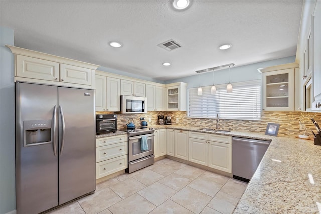 kitchen featuring light stone countertops, stainless steel appliances, sink, pendant lighting, and cream cabinets