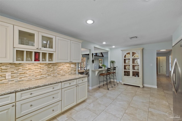 kitchen with stainless steel fridge, backsplash, light stone counters, and light tile patterned flooring