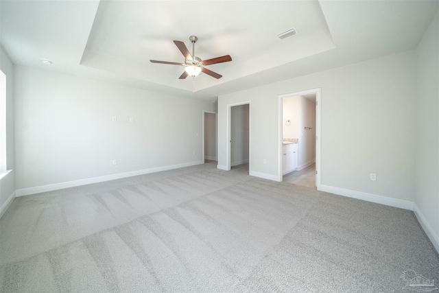 unfurnished bedroom with a tray ceiling, ceiling fan, and ensuite bathroom