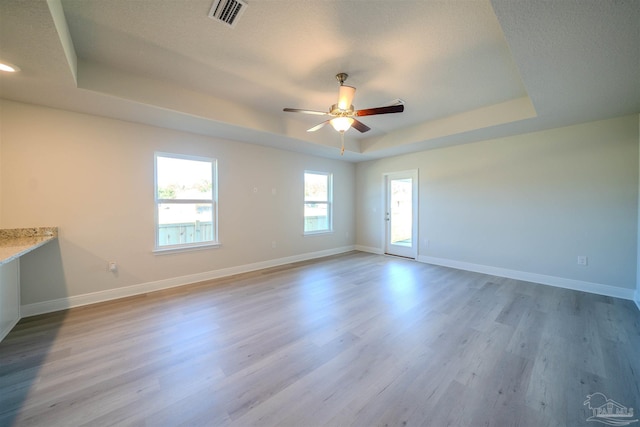 empty room featuring ceiling fan, light hardwood / wood-style floors, and a tray ceiling