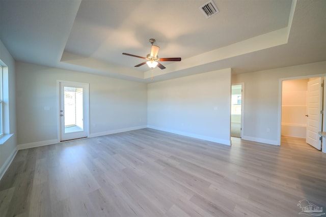 empty room with light hardwood / wood-style floors, a raised ceiling, and ceiling fan