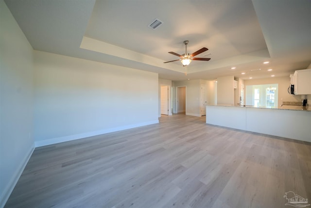 unfurnished living room with sink, a raised ceiling, ceiling fan, and light wood-type flooring