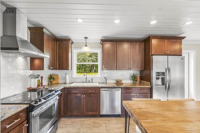 kitchen featuring light stone countertops, wall chimney exhaust hood, tasteful backsplash, a sink, and stainless steel appliances