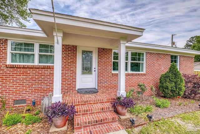 view of exterior entry with brick siding and crawl space