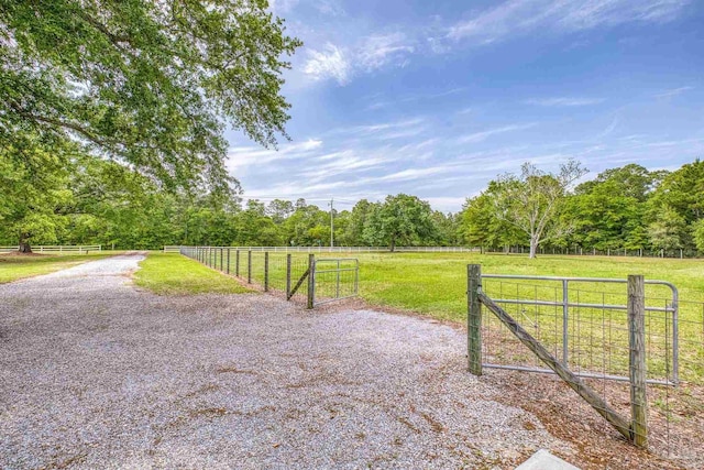 view of gate with a lawn, a rural view, fence, and a wooded view