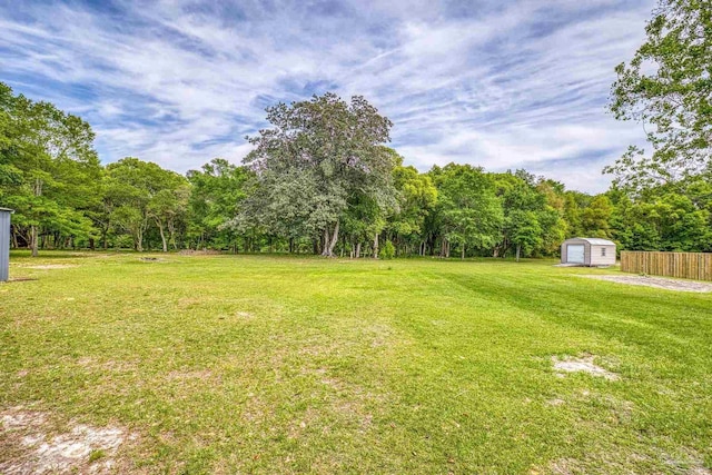view of yard featuring a storage shed, an outbuilding, a detached garage, a view of trees, and fence