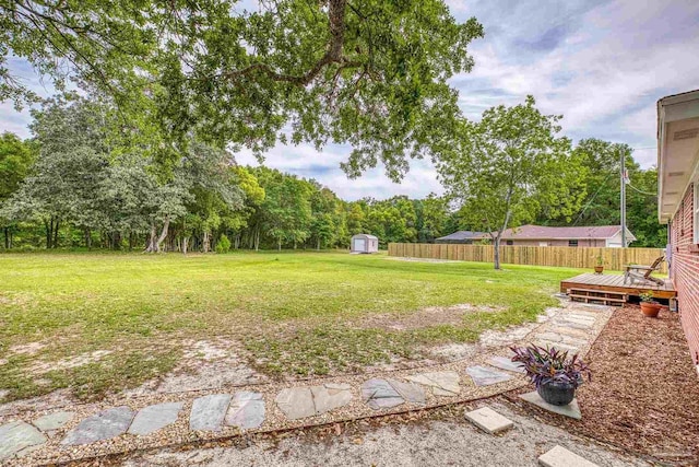 view of yard featuring fence, a storage unit, an outbuilding, and a deck