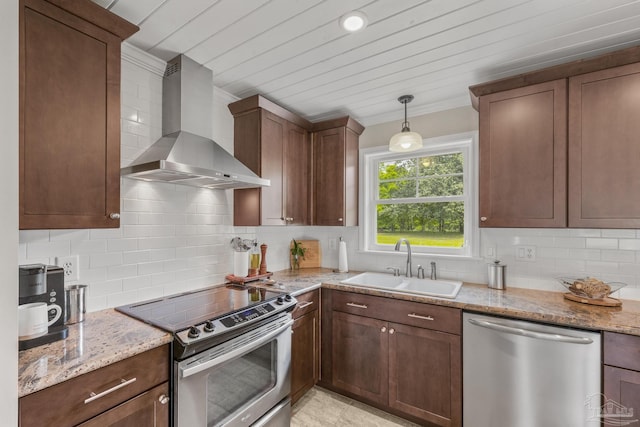 kitchen featuring decorative backsplash, light stone countertops, wall chimney exhaust hood, a sink, and appliances with stainless steel finishes