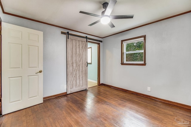 unfurnished bedroom featuring a barn door, a ceiling fan, baseboards, wood finished floors, and ornamental molding