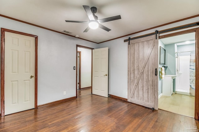 unfurnished bedroom featuring visible vents, a barn door, baseboards, and wood finished floors