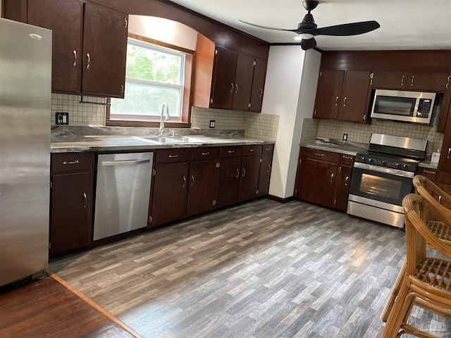 kitchen with decorative backsplash, a sink, wood finished floors, a ceiling fan, and appliances with stainless steel finishes