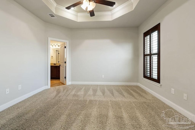 empty room with baseboards, visible vents, a raised ceiling, light colored carpet, and crown molding