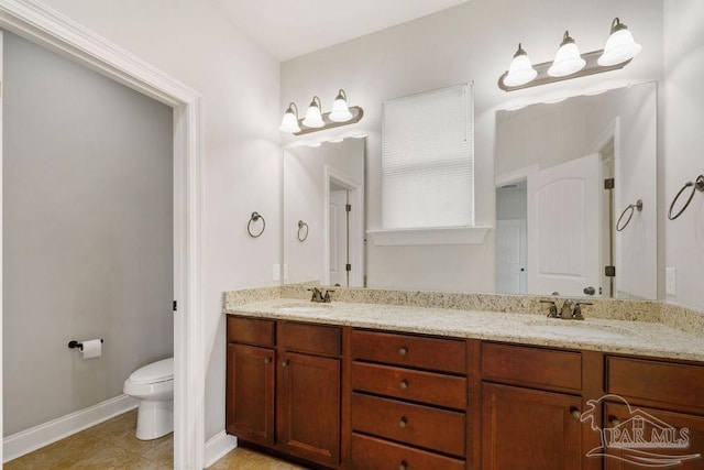 bathroom featuring toilet, double vanity, baseboards, and a sink