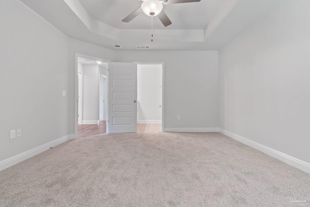 unfurnished room with a raised ceiling, light carpet, and ceiling fan