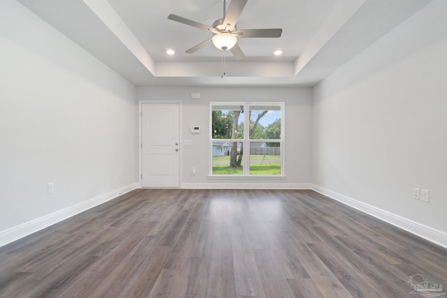 unfurnished room featuring a tray ceiling, dark wood-type flooring, and ceiling fan