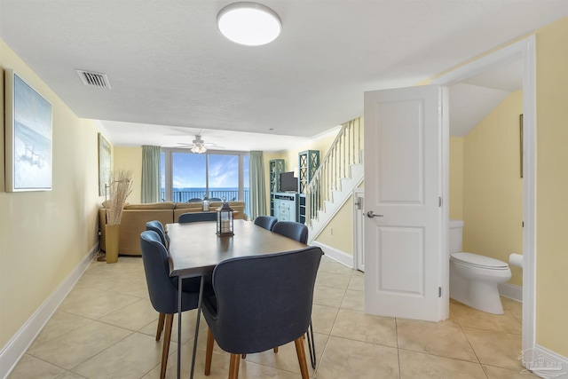 dining room featuring light tile patterned floors, a ceiling fan, visible vents, baseboards, and stairway