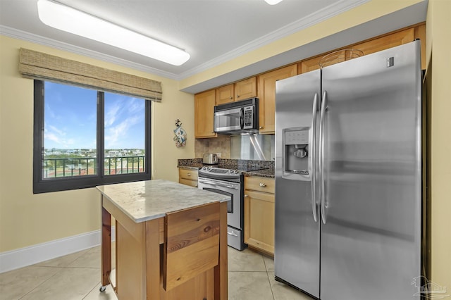 kitchen with light tile patterned floors, appliances with stainless steel finishes, a kitchen island, and ornamental molding