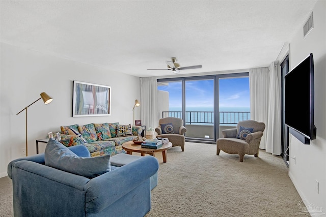 living room with a textured ceiling, light colored carpet, expansive windows, and ceiling fan