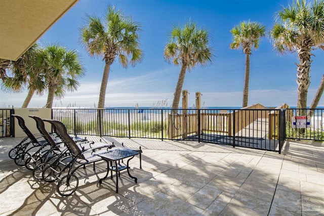 view of patio featuring a balcony, a beach view, and a water view