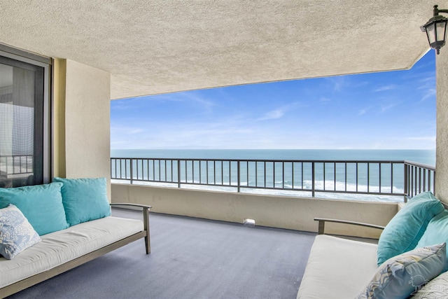 balcony featuring an outdoor living space, a water view, and a view of the beach