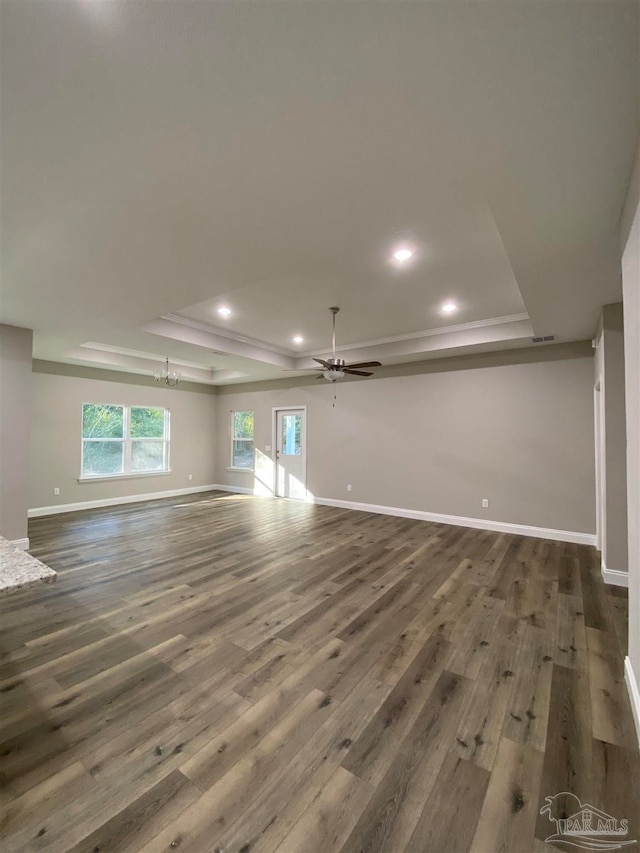 unfurnished living room with a tray ceiling, ceiling fan with notable chandelier, and dark hardwood / wood-style floors