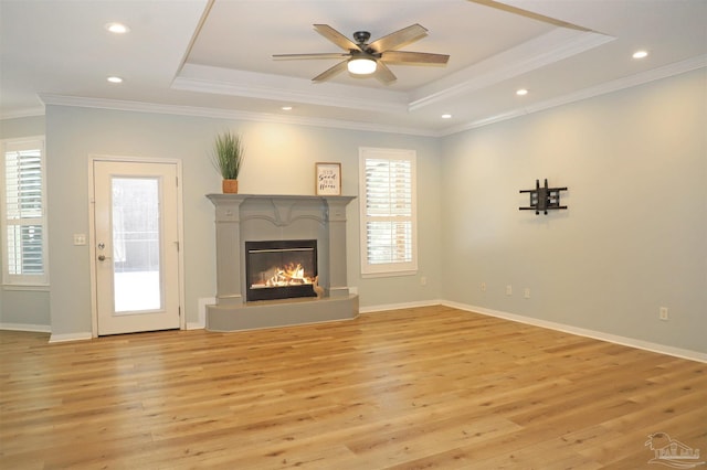 unfurnished living room featuring ornamental molding, a tray ceiling, a glass covered fireplace, and light wood-style flooring