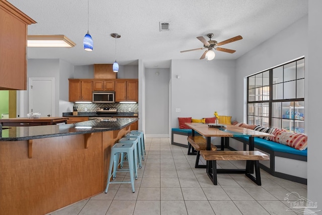 3849 Saber Tooth Cir, Gulf Breeze, FL 32563 - kitchen featuring appliances with stainless steel finishes, brown cabinetry, a kitchen bar, backsplash, and a ceiling fan