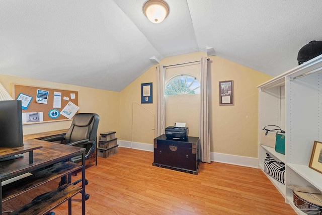 home office featuring lofted ceiling, light wood-type flooring, and a textured ceiling