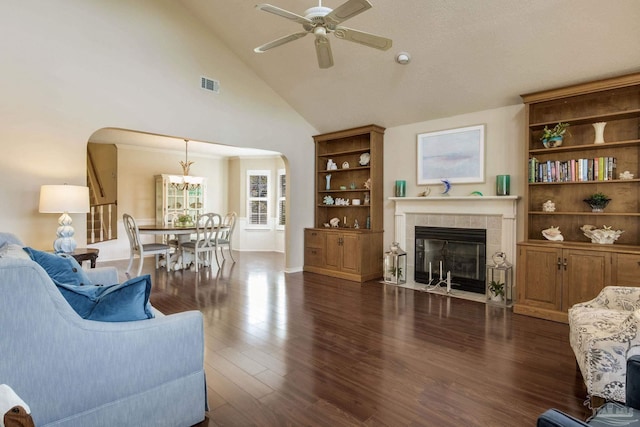 living area with visible vents, ceiling fan with notable chandelier, a fireplace, arched walkways, and dark wood-style flooring