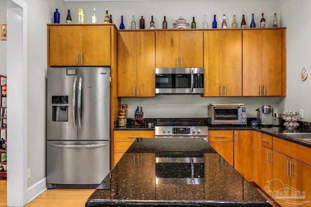 kitchen featuring dark stone countertops, stainless steel appliances, and light wood-type flooring