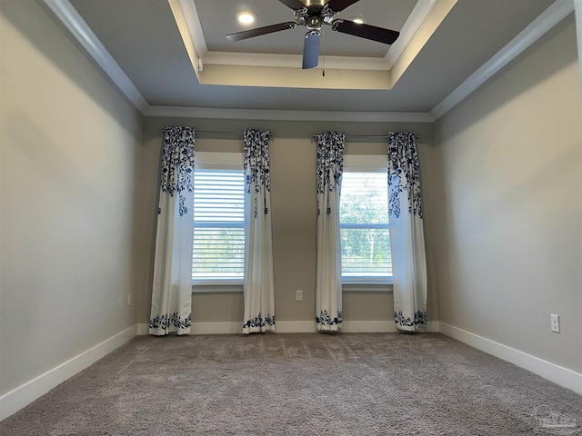 carpeted spare room featuring ceiling fan, a wealth of natural light, ornamental molding, and a raised ceiling