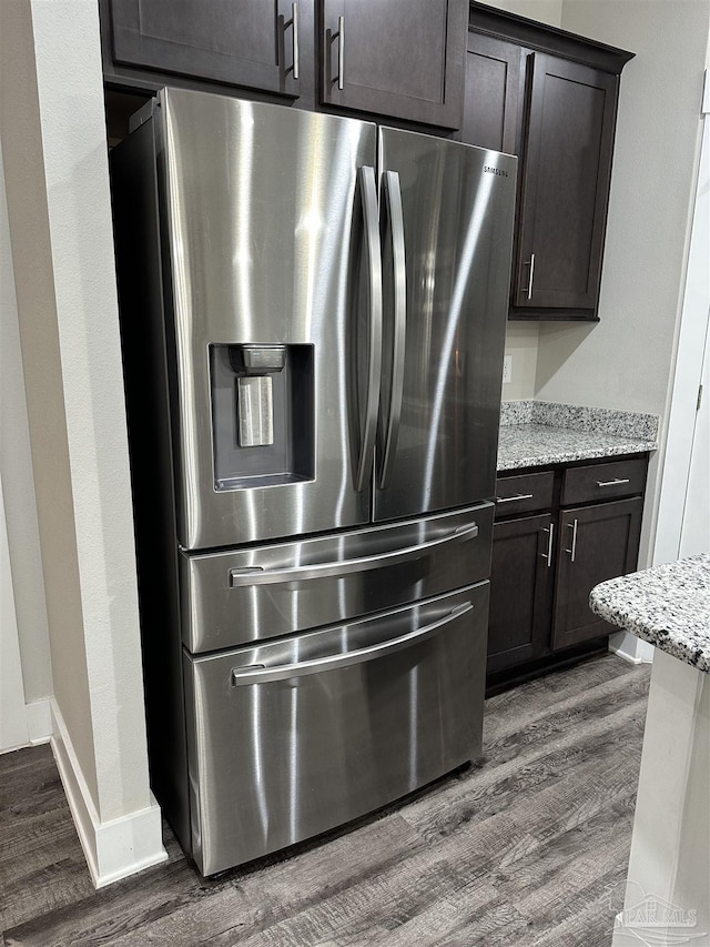 room details with light stone counters, hardwood / wood-style flooring, dark brown cabinetry, and stainless steel fridge