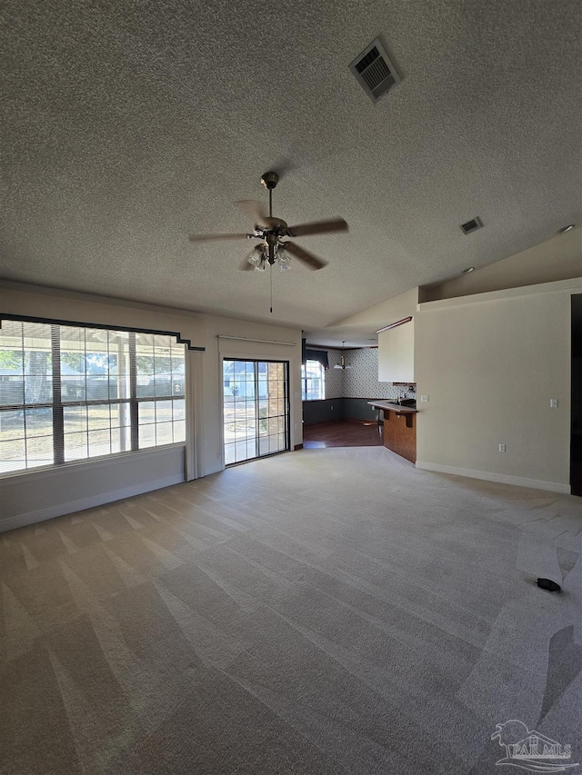 unfurnished living room with ceiling fan, vaulted ceiling, carpet, and a textured ceiling