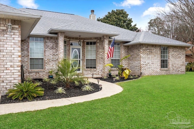 view of front of home with brick siding, a chimney, a front lawn, and roof with shingles