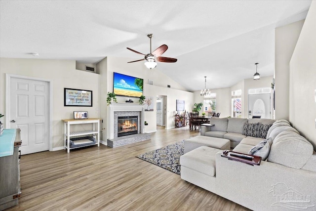 living area with ceiling fan with notable chandelier, a fireplace, wood finished floors, visible vents, and vaulted ceiling