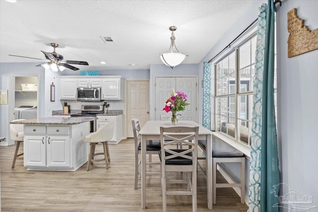 dining room featuring a textured ceiling, ceiling fan, visible vents, washer and dryer, and light wood finished floors