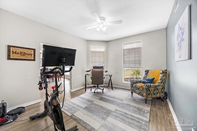 office space featuring a ceiling fan, a textured ceiling, baseboards, and wood finished floors