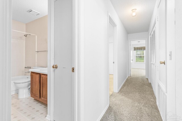 hallway featuring light colored carpet and a textured ceiling